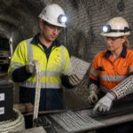 A mining safety engineer and a miner inspect high strength fiber rope and fiber reinforced mesh inside an underground mine tunnel.